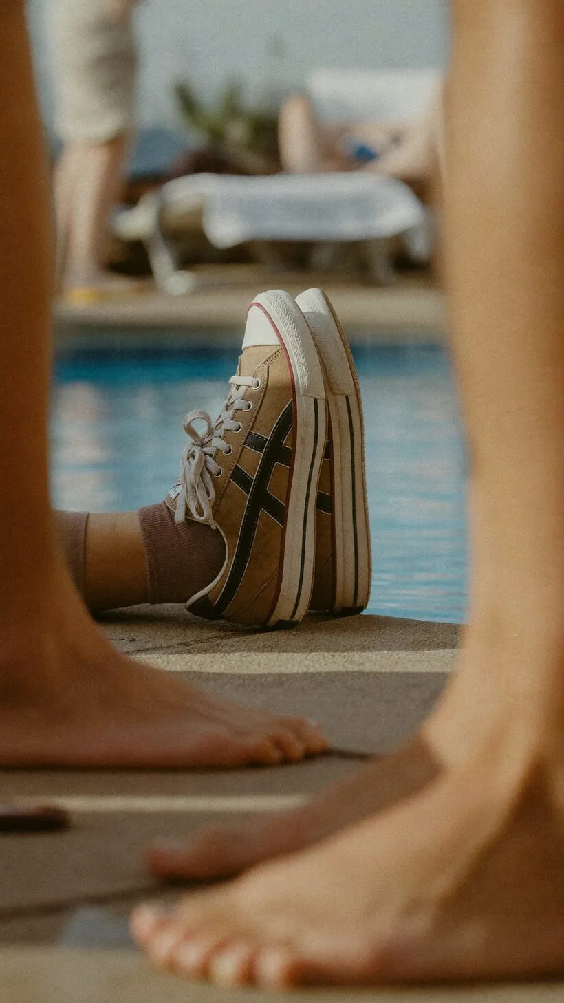 Person keeping their sneakers on by the pool while others are barefoot